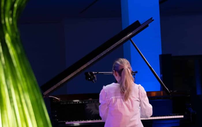 Pianist Johanna Summer plays a grand piano under blue lighting, a green sculpture in the foreground.