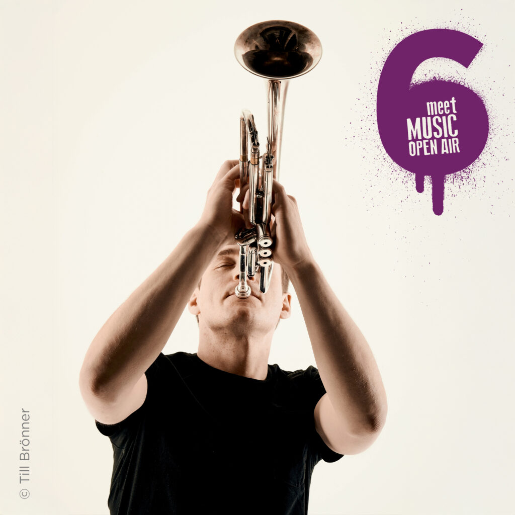 Bill Petry in schwarzem Hemd spielt Trompete, in der rechten Ecke des Bildes ist das meetMUSIC Open Air Logo zu sehen.