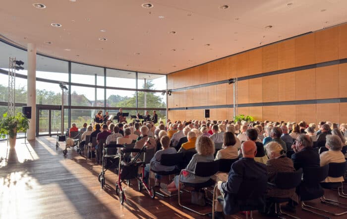 Das Publikum genießt ein Septett beim Summerwinds-Festival in einem sonnendurchfluteten Saal mit großen Fenstern.