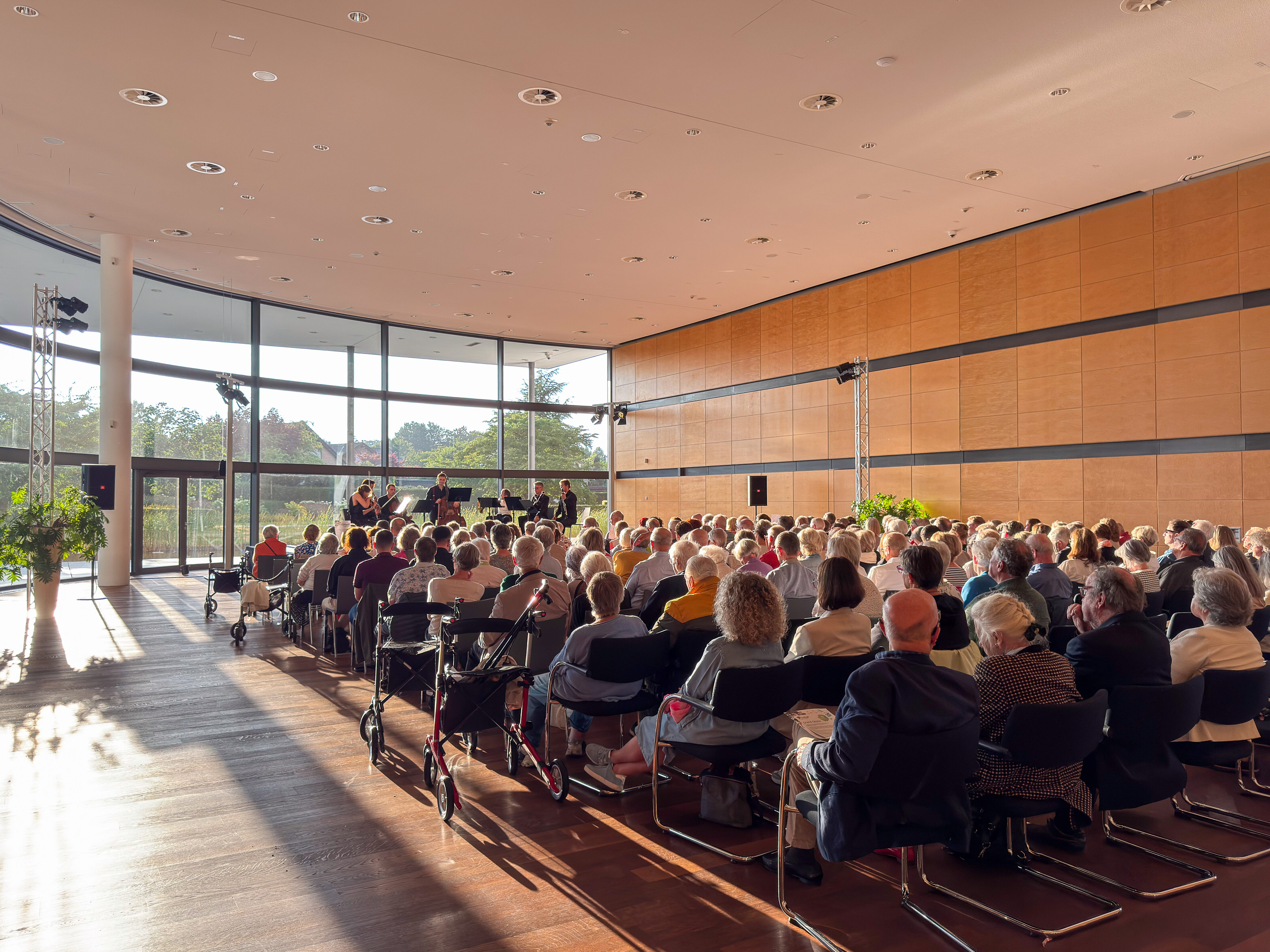Das Publikum genießt ein Septett beim Summerwinds-Festival in einem sonnendurchfluteten Saal mit großen Fenstern.