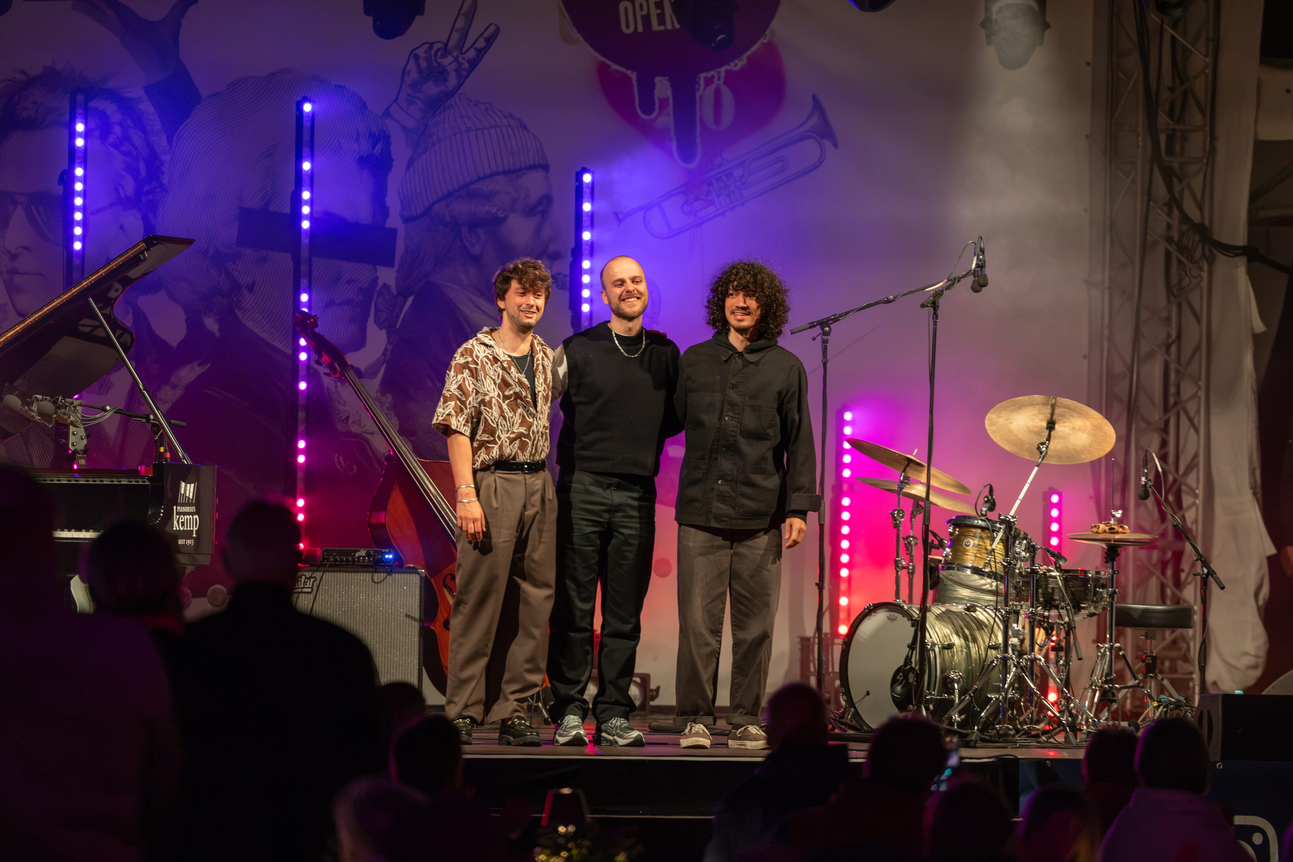 Das Luca-Sestak-Trio tritt auf der Bühne des meetMUSIC Open Air auf, während violettes Licht leuchtet.