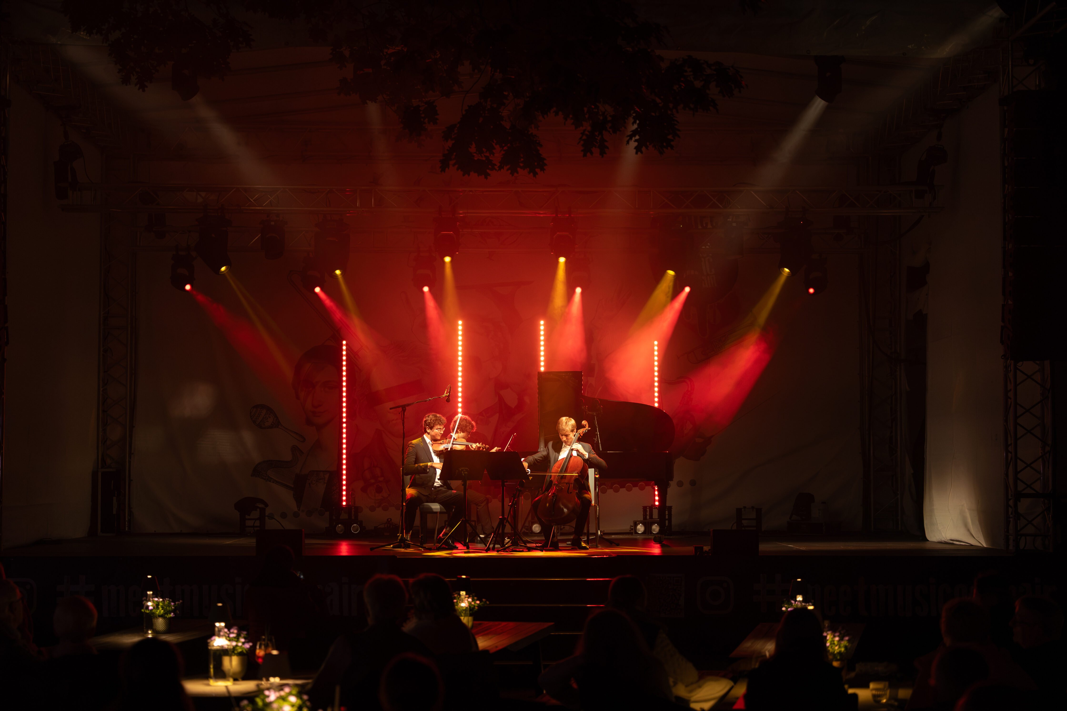 Das Trio Jaspard tritt auf der Bühne mit Klavier und Cello auf, beleuchtet von rotem und gelbem Licht.