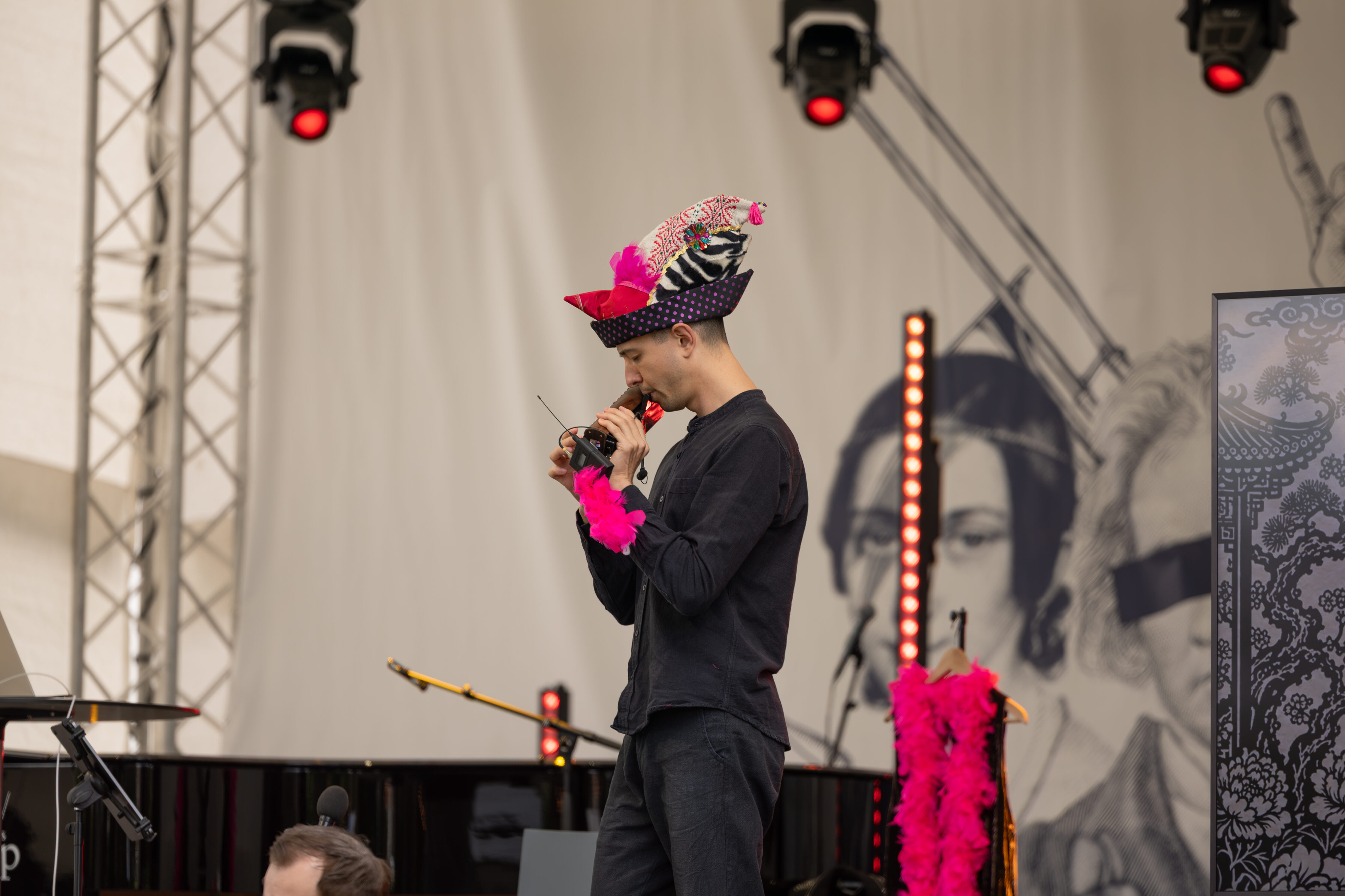 Nico, der einen bunten Hut und eine rosa Boa trägt, hält auf der Bühne des meetMUSIC Open Air eine Rede.